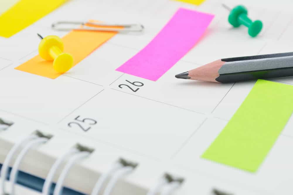 A calendar planner with colorful sticky notes and a black pencil.