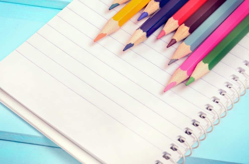 A bullet journal or notebook with colored pencils and a bright blue background.