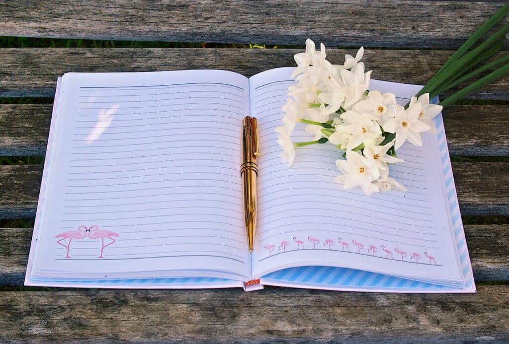 A bullet journal with flowers and a gold pen on a wooden table.