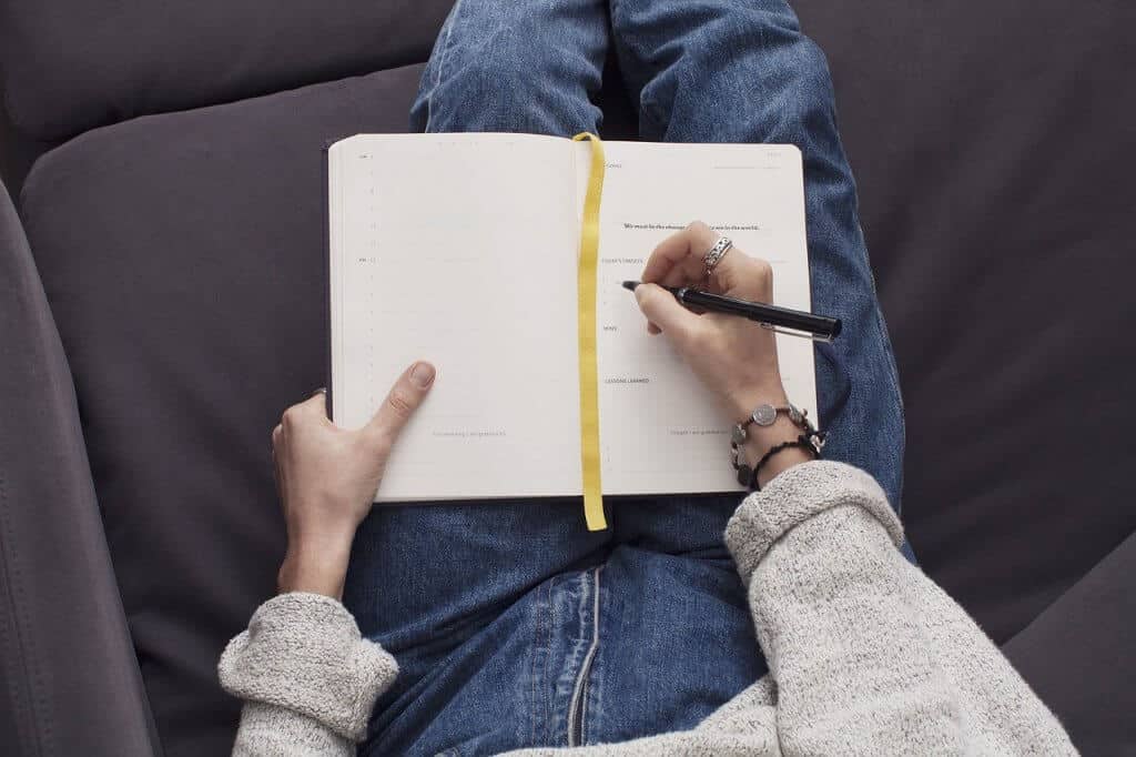 A woman journaling in a notebook with a black pen and gold ribbon.