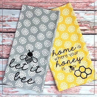 Two tea towels with honey bee quotes on a painted wood background.
