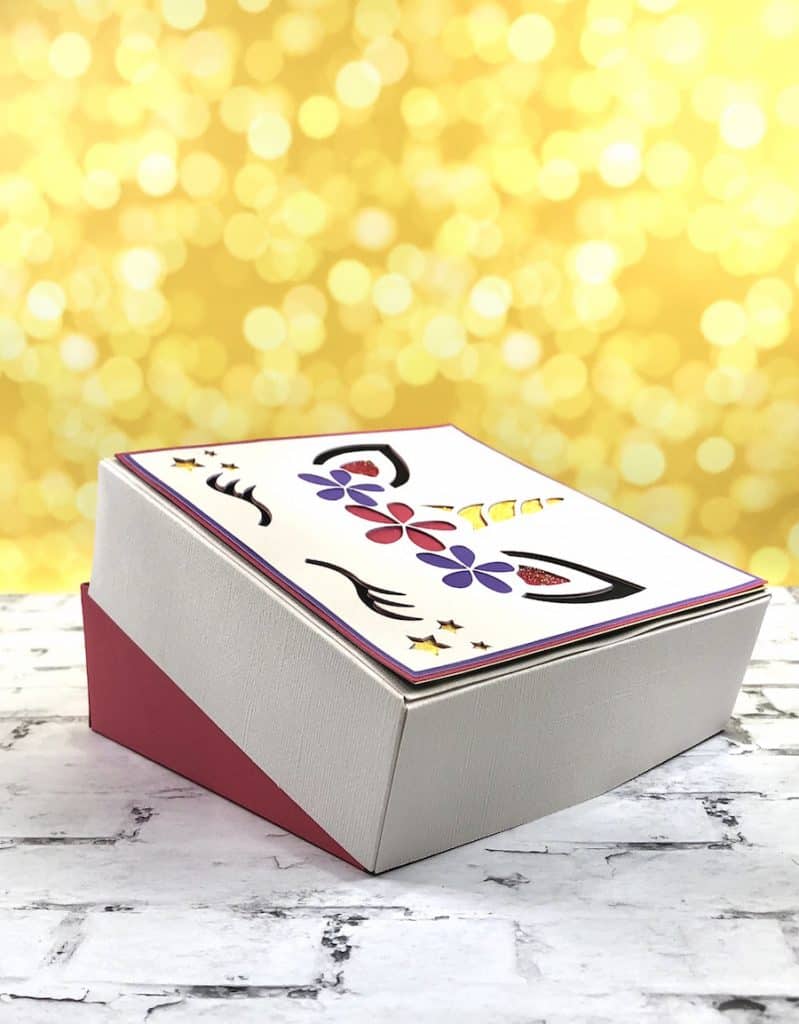 Side view of a colorful unicorn paper box on a white brick background.